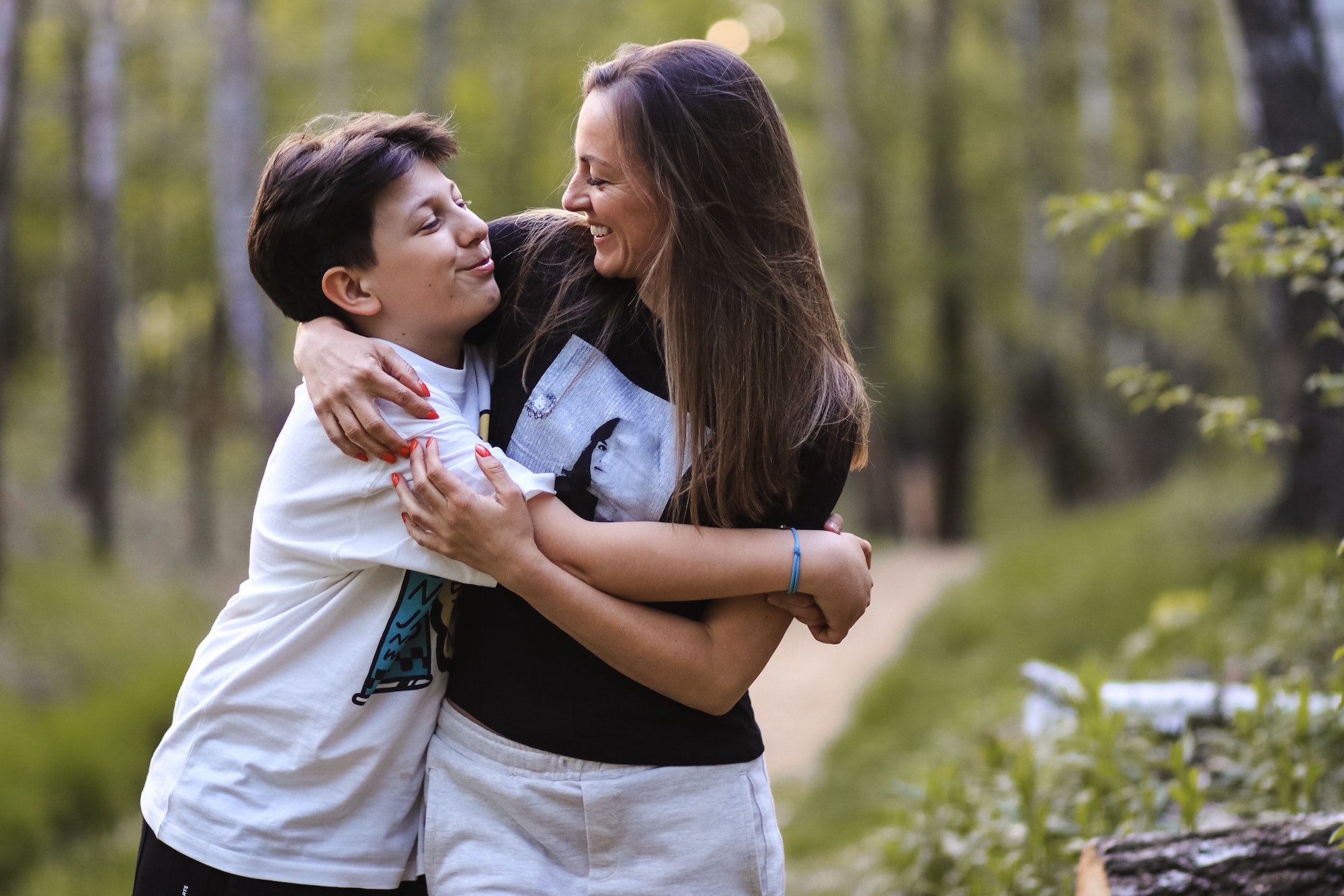 Mom and son having fun in the park in the spring time. Parents and teen. Teenage boy hugs mom.