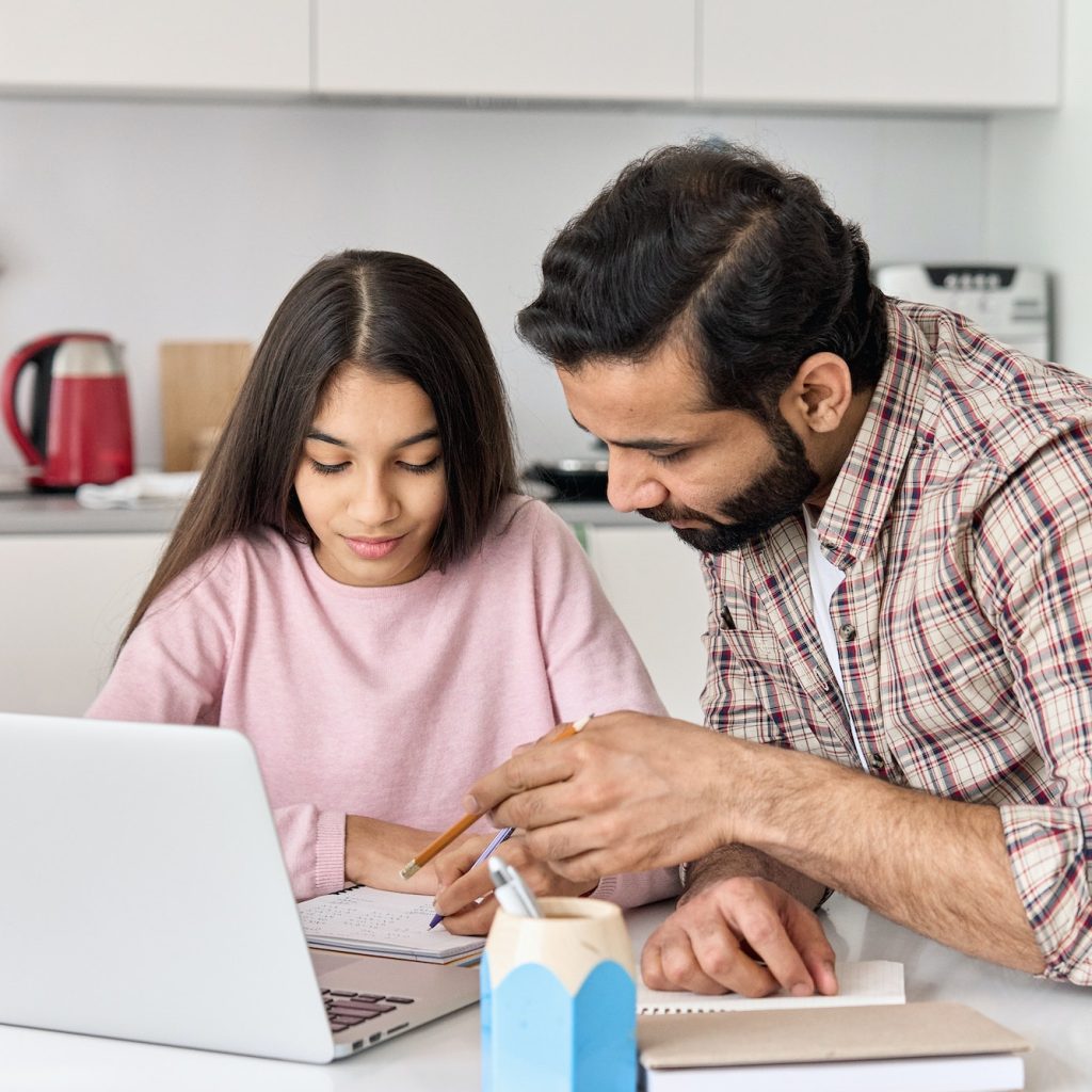 Indian parent dad helping school child teen daughter studying online at home.